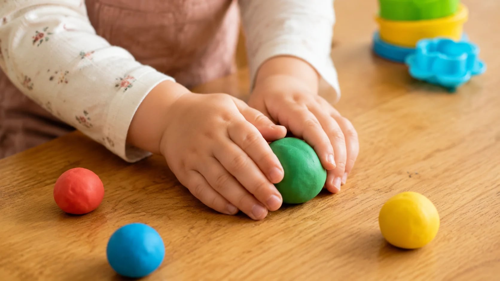 Ребёнок 4-5 лет катает разноцветный пластилин на деревянной столешнице
