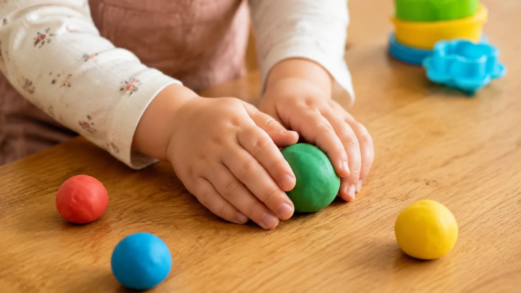 Ребёнок 4-5 лет катает разноцветный пластилин на деревянной столешнице